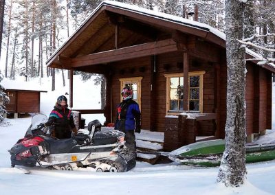 Moottorikelkkailijoita mökin edessä moottorikelkan kanssa.