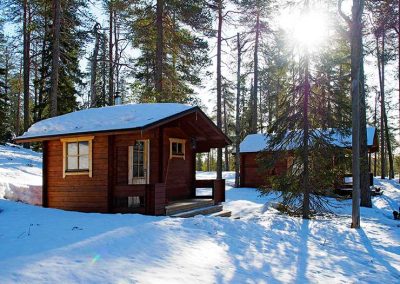 Hirsiseinäiset sauna ja mökki kevätauringon paisteessa.