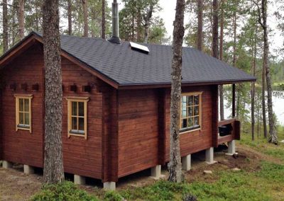 Punaruskeaseinäinen mökki järvenrannassa kesällä.