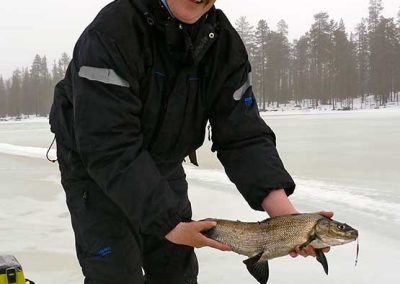 Hymyilevä mies jäällä pilkitty siika käsissään.